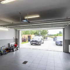 Wnętrze nowoczesnego domu z garażem w piwnicy. W garażu stoją dwa samochody, a obok nich dziecięce pojazdy.