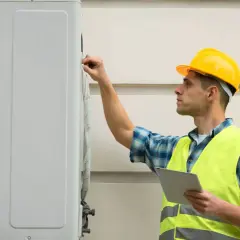 Technik w żółtym kasku i kamizelce odblaskowej sprawdza pompę ciepła. Serwis klimatyzacji w toku.
