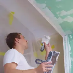 Mężczyzna nakłada gips na sufit. Czas schnięcia tynku gipsowego zależy od warunków.