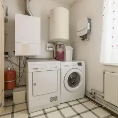 Pomieszczenie gospodarcze z pralką, suszarką, bojlerem i szafą.