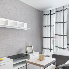 Nowoczesny salon z szarą ścianą pokrytą tynkiem japońskim o subtelnych wzorach. Białe meble i zasłony w kratę dodają lekkości.