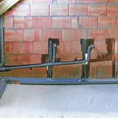 Instalacja hydrauliczna w trakcie budowy. Widoczny pion sanitarny z rurami i kolankami, przygotowany do dalszych prac.