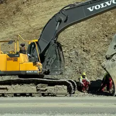 Dwa rodzaje koparek, w tym żółta Volvo EC220DL, pracują przy osuwisku. Dwóch robotników w kamizelkach odblaskowych odpoczywa.