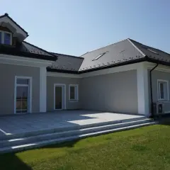 Elegancki dom z tarasem i trawnikiem. Biały gzyms podkreśla architekturę budynku.