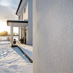 Biały, chropowaty tynk strukturalny na ścianie domu, w zimowej scenerii ze śniegiem i zachodzącym słońcem.