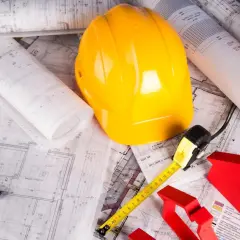 Plany domu, żółty kask, miarka i poziomica – wszystko gotowe do samodzielnej budowy domu.