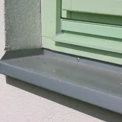 Szary parapet zewnętrzny zamontowany przy zielonym oknie. Pokazuje detale, jak zamontować parapet zewnętrzny.