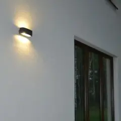 Nierówności na elewacji pod światło. Dwa kinkietowe punkty świetlne oświetlają białą, chropowatą ścianę domu, tworząc subtelne cienie.