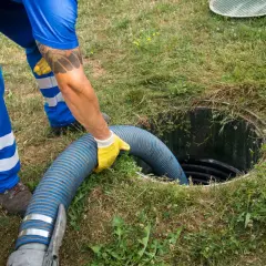 Pracownik w żółtych rękawiczkach wkłada gruby wąż do szamba, pokazując, jak zrobić odpływ.