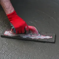 Ręka w czerwonej rękawicy wygładza świeży beton. To kluczowy etap prac, który wpływa na to, jaka grubość posadzki w garażu będzie optymalna.