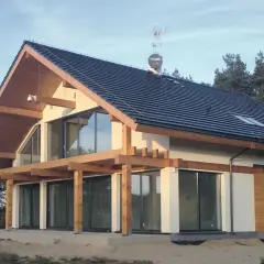Nowoczesny dom z gotowych elementów, z drewnianą konstrukcją i dużymi przeszkleniami, otoczony lasem.