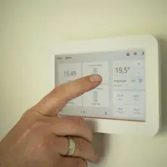 Dłoń dotyka ekranu termostatu, który pokazuje temperaturę 19,5°C. To nowoczesne rozwiązanie, które może być częścią systemu z piecem kondensacyjnym.