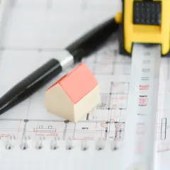 Miniaturowy domek, długopis i miarka na planach architektonicznych. Wszystko gotowe do uzyskania pozwolenia na budowę.