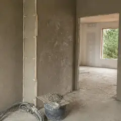 Ściany pokryte tynkami gipsowymi, widoczny fragment pionowej konstrukcji z listwami. W wiadrze zaprawa i kielnia.
