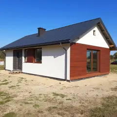 Nowy dom szkieletowy na zgłoszenie, z białym tynkiem i drewnianą elewacją, gotowy do zamieszkania.