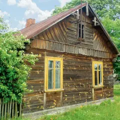 Stary, drewniany dom z żółtymi oknami, otoczony zielenią. Wnętrze tego domu kryje zapewne wiele historii.