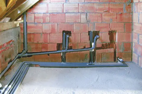 Instalacja hydrauliczna w trakcie budowy. Widoczny pion sanitarny z rurami i kolankami, przygotowany do dalszych prac.