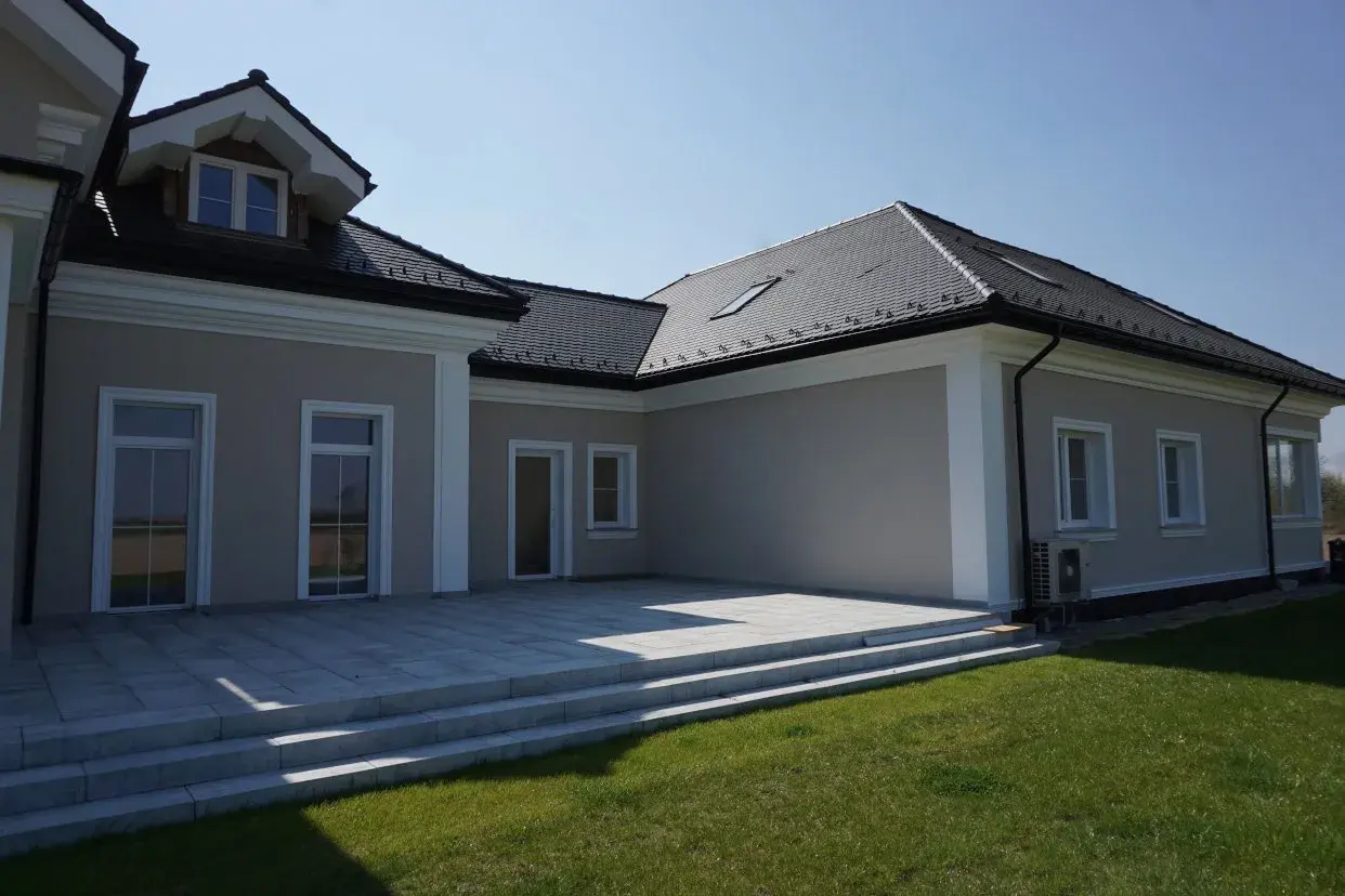 Elegancki dom z tarasem i trawnikiem. Biały gzyms podkreśla architekturę budynku.