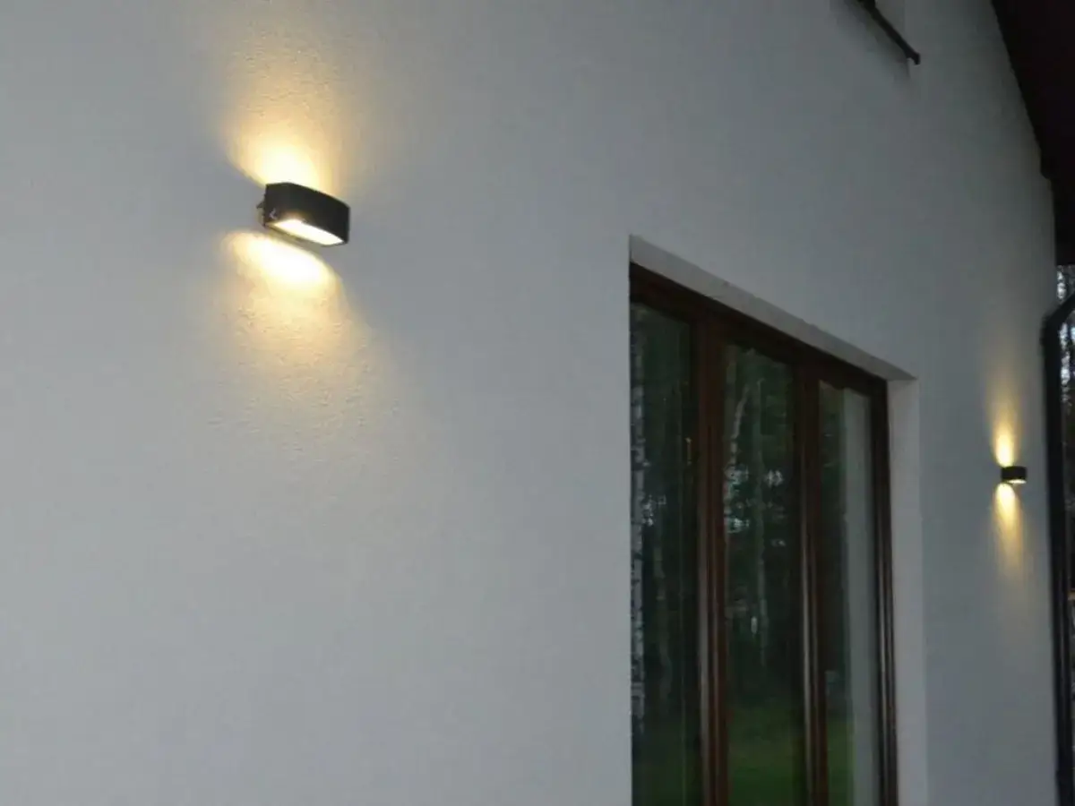 Światło lamp podkreśla nierówności na elewacji, tworząc subtelne cienie. Widać okno i fragment dachu.
