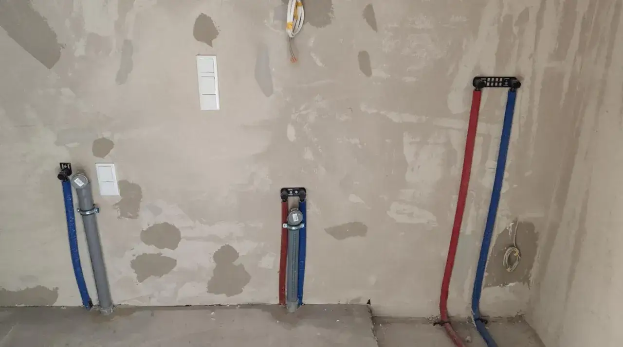 Instalacja wodna w trakcie prac. Wkuwanie rur w ścianę przepisy są kluczowe dla bezpieczeństwa i funkcjonalności. Widać instalację wodną z rurami wodnymi i kanalizacyjnymi.