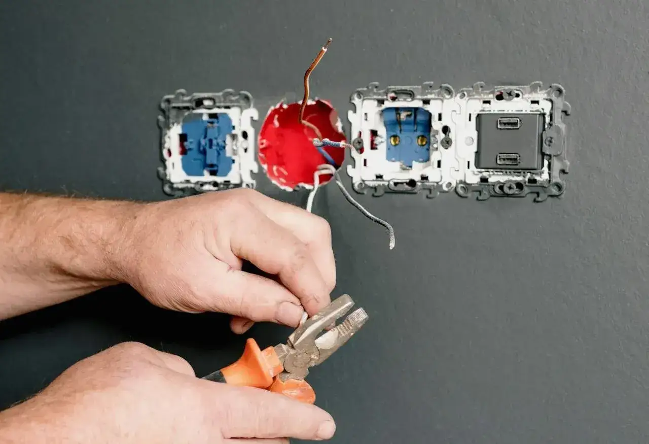 Ręce elektryka podczas montażu gniazdka. Przygotowuje przewody do podłączenia, używając kombinerki.